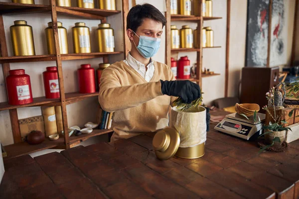 Mannelijke werknemer in medisch masker met een gewicht van thee bladeren — Stockfoto