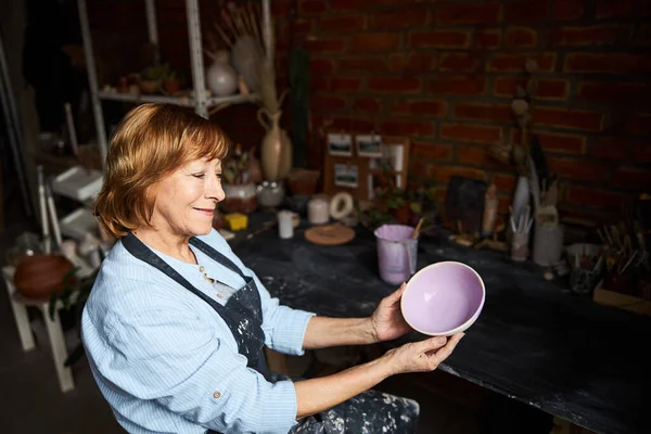 Encantadora anciana sosteniendo cuenco pintado en taller de cerámica —  Fotos de Stock