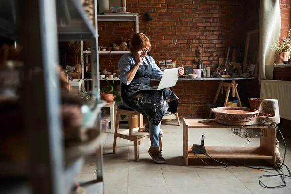 Mulher idosa encantadora usando laptop na oficina de cerâmica — Fotografia de Stock