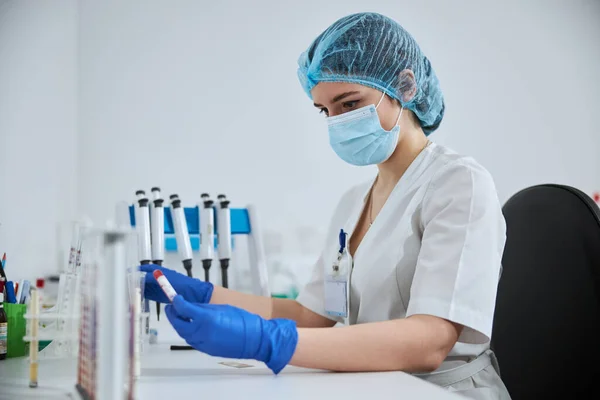 Técnico de laboratório sério examinando uma amostra clínica em sua mão — Fotografia de Stock