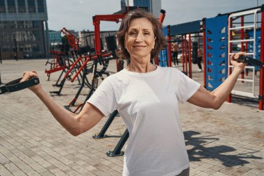 Spor sahasında kollarını çalıştıran neşeli olgun bir bayan.