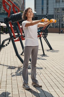 Mutlu olgun kadın açık havada omuzlarını çalıştırıyor.