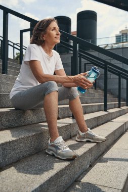 Dışarıda merdivenlerde oturan rahat, aktif yaşlı bir kadın.