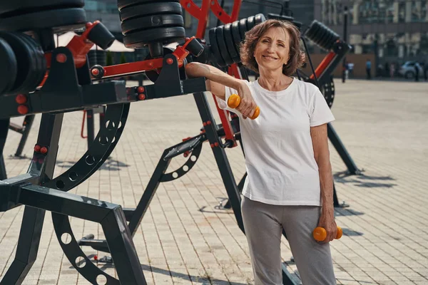 Joyful aged female enjoying training with dumbbells outdoors —  Fotos de Stock