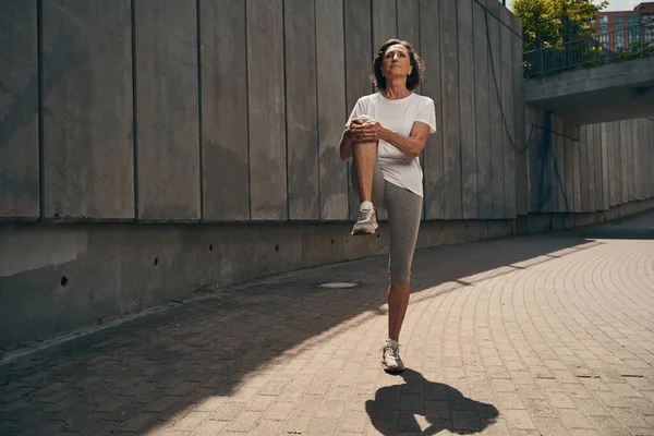 Весела літня жінка розтягує ноги після тренування — стокове фото