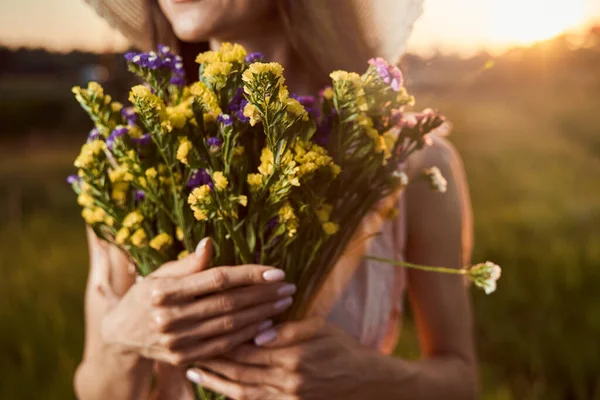 Lila och gula blommor i händerna på ung kvinna — Stockfoto