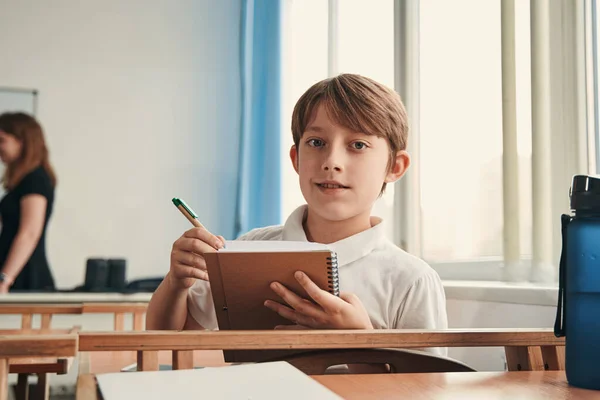 Confident pupil sitting by the window in his classroom — Stock Photo, Image