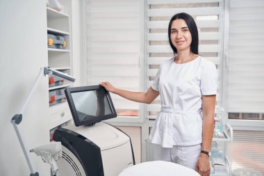 Modern tıp ofisinde gülümseyen genç kozmetik uzmanı.