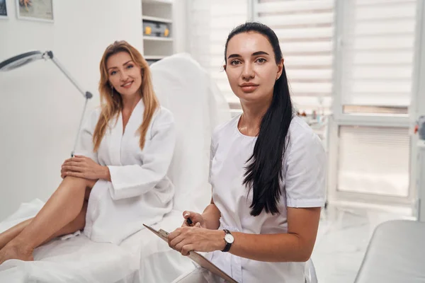 Cosmetologista feminino alegre com cliente no escritório — Fotografia de Stock