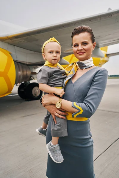 Pretty stewardess and her child posing against the landed airliner — Stock Photo, Image