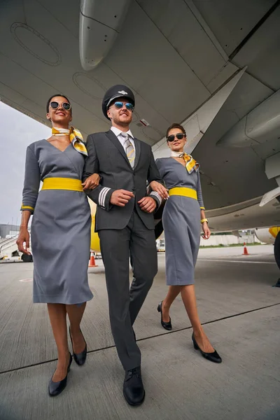 Pleased airman accompanied by dark-haired stewardesses going ahead — Stock Photo, Image