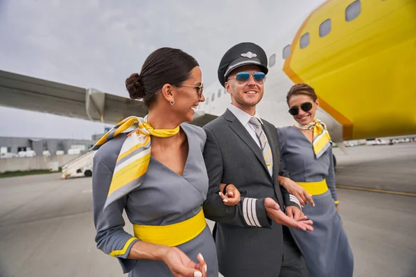 Aviator and two joyous flight attendants by a landed aircraft — Stock Photo, Image