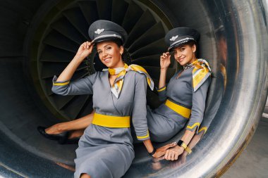 Two stewardesses posing for the camera seated in the aeroengine clipart