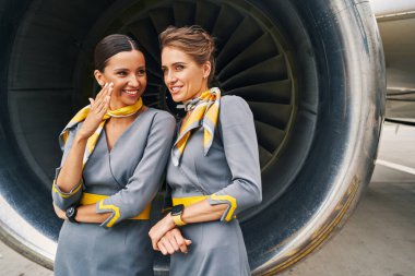 Üniformalı iki hostes aeromotorun yanında sohbet ediyor.