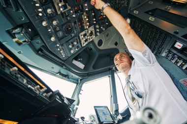 Male pilot flipping a switch on the overhead control panel clipart