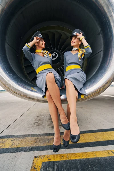 Hospedeiras alegres em bonés pilotos sentados de pernas cruzadas no aeromotor — Fotografia de Stock