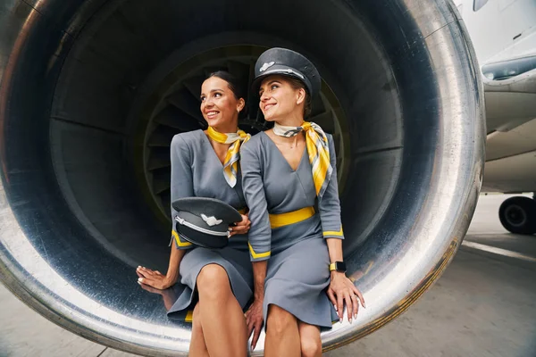 Two pretty stewardesses in uniforms sitting in the aeroengine — Stock Photo, Image