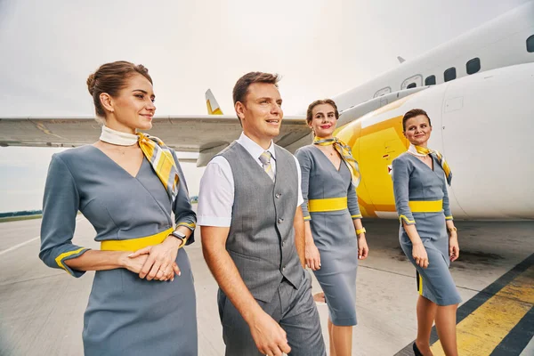 Cuatro atractivos miembros de la tripulación junto a un avión de tierra — Foto de Stock