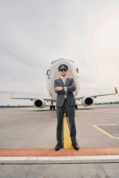 Tranquil aviator in uniform poserend tegen een landingsvliegtuig — Stockfoto