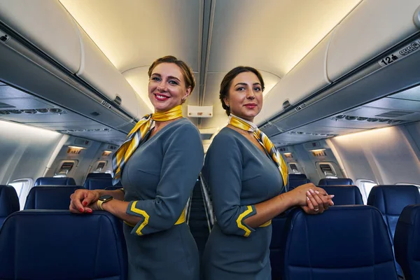 Azafata sonriente y su colega apoyándose en los asientos de la aerolínea — Foto de Stock