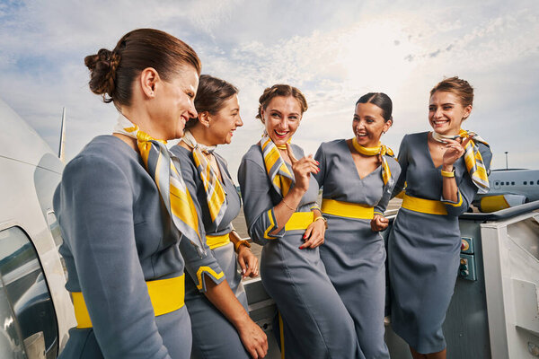Joyful stewardesses standing on the boarding stairs during the conversation