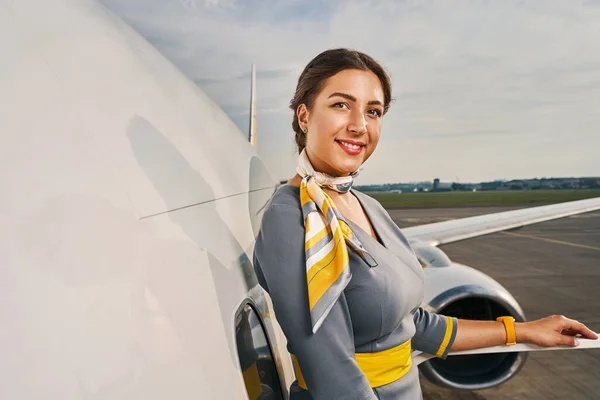 Удовольственная стюардесса позирует перед камерой у самолета — стоковое фото