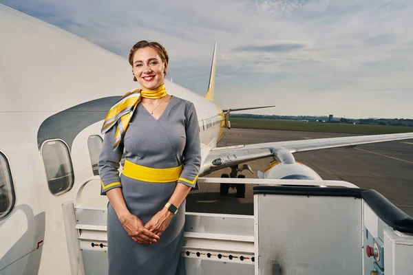 Radostná letuška v uniformě stojící u přistávajícího letadla — Stock fotografie
