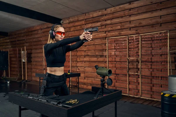Donna concentrata in paraorecchie e occhiali di sicurezza sparare una pistola — Foto Stock