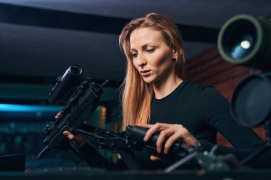 Kadın tetikçi silahının parçalarını birleştirmeye odaklanmış.