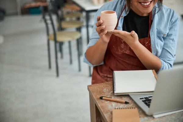 Радісний жіночий гончар використовує ноутбук у керамічній майстерні — стокове фото