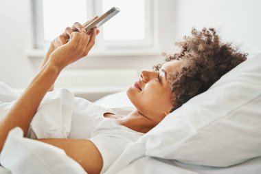 Yatakta mesaj yazan gülümseyen kadın.