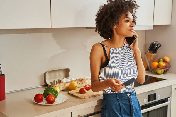 Cute female cook having a phone conversation in the kitchen