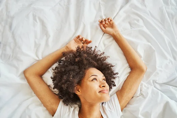 Cute lady with thick dark curly hair daydreaming in bed — ストック写真