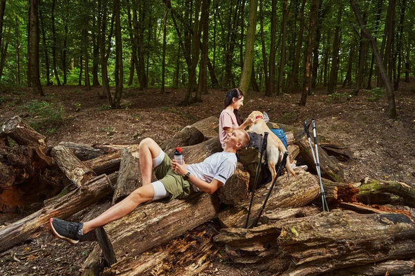 Улыбающаяся активная пара отдыхает с домашним животным в лесу — стоковое фото