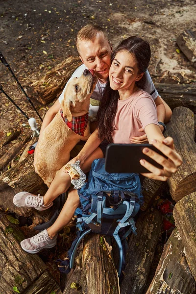 Coppia gioiosa con cane scattare selfie in legno — Foto Stock