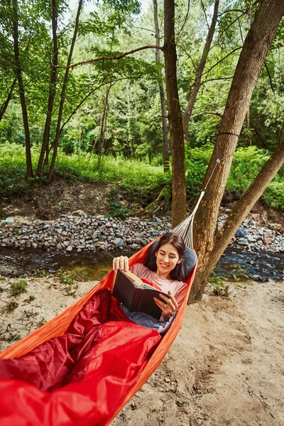 Sorridente giovane donna che legge vicino riva del fiume — Foto Stock