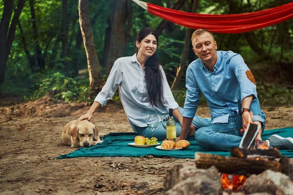 Happy couple with dog on picnic in forest — Stock Photo, Image