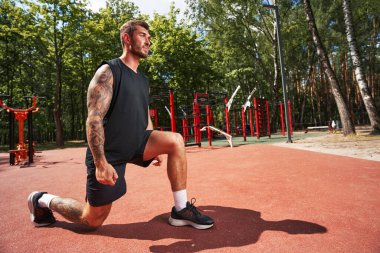 Atletik dövmeli adam spor sahasında tek başına egzersiz yapıyor.