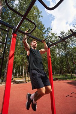 Kaslı sakallı adam dışarıda vücut geliştiriyor.