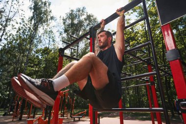 Genç sakallı erkek dışarıda karın kaslarını çalıştırıyor.