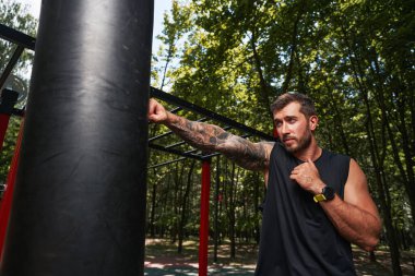 Genç dövmeli adam spor sahasında boks yapıyor.