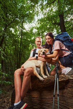 Neşeli çift ormanda köpekle kucaklaşıyor.