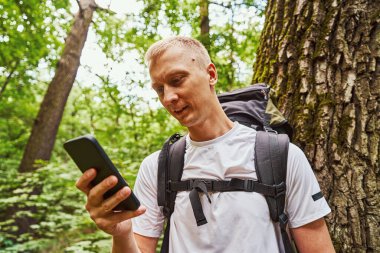 Mutlu genç adam yeşil ormanda mesajlaşıyor.