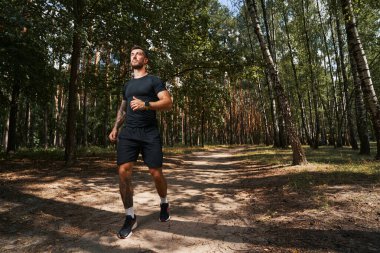 Yeşil ormanda koşan sakin atletik adam