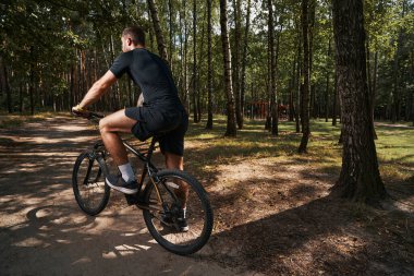 Atletik genç adam ormanda bisiklete biniyor.