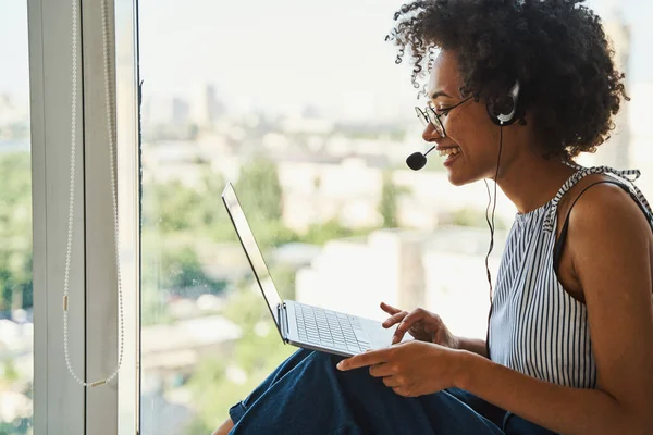 Glad kvinna i hörlurar med en mikrofon som kommunicerar online — Stockfoto