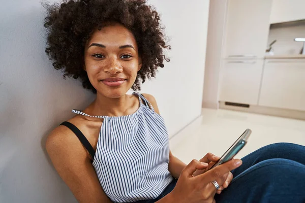 Nöjd kvinna med smartphone lutade sig tillbaka mot väggen — Stockfoto