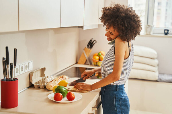 Female cutting vegetables on the board during the phone call
