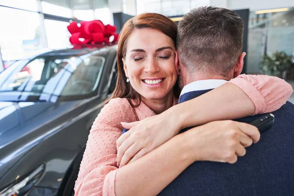Dankbare Frau umarmt ihren Mann im Autohaus — Stockfoto