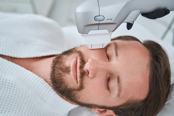 Homem de cabelos escuros barbudo e bigode a dormir durante um procedimento de elevação facial não invasivo — Fotografia de Stock